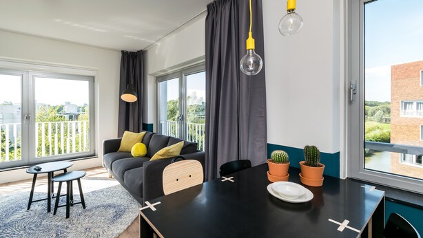 A modern living room with a sofa, a dining table, and a large window with curtains. - StudentStay (Leeuwarden)