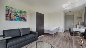 A modern hotel room with a sofa, a bed, a dining table, and a painting of a cityscape. - StudentStay (Leeuwarden)