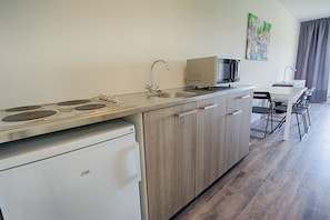 A compact kitchenette with a stove, microwave, and refrigerator. - StudentStay (Leeuwarden)