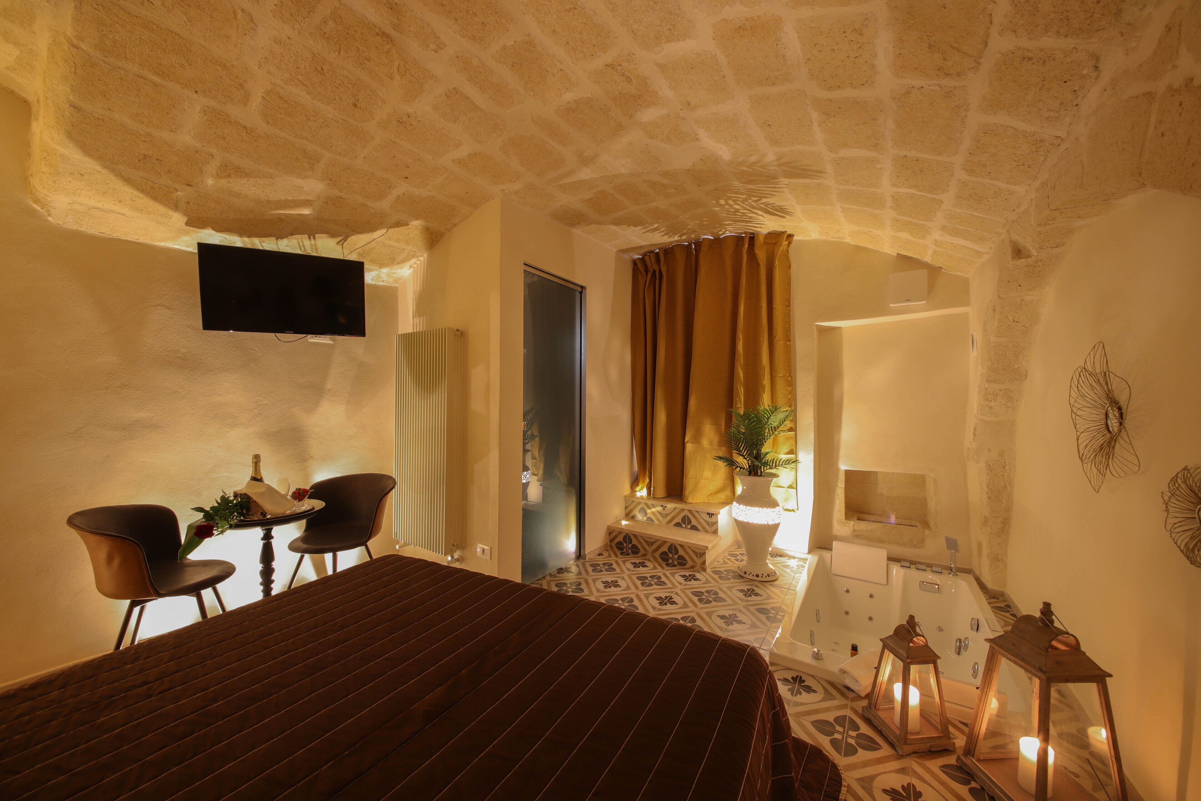 A bedroom with a large bed, a desk with chairs, a television, a bathroom with a bathtub, and a window with curtains.