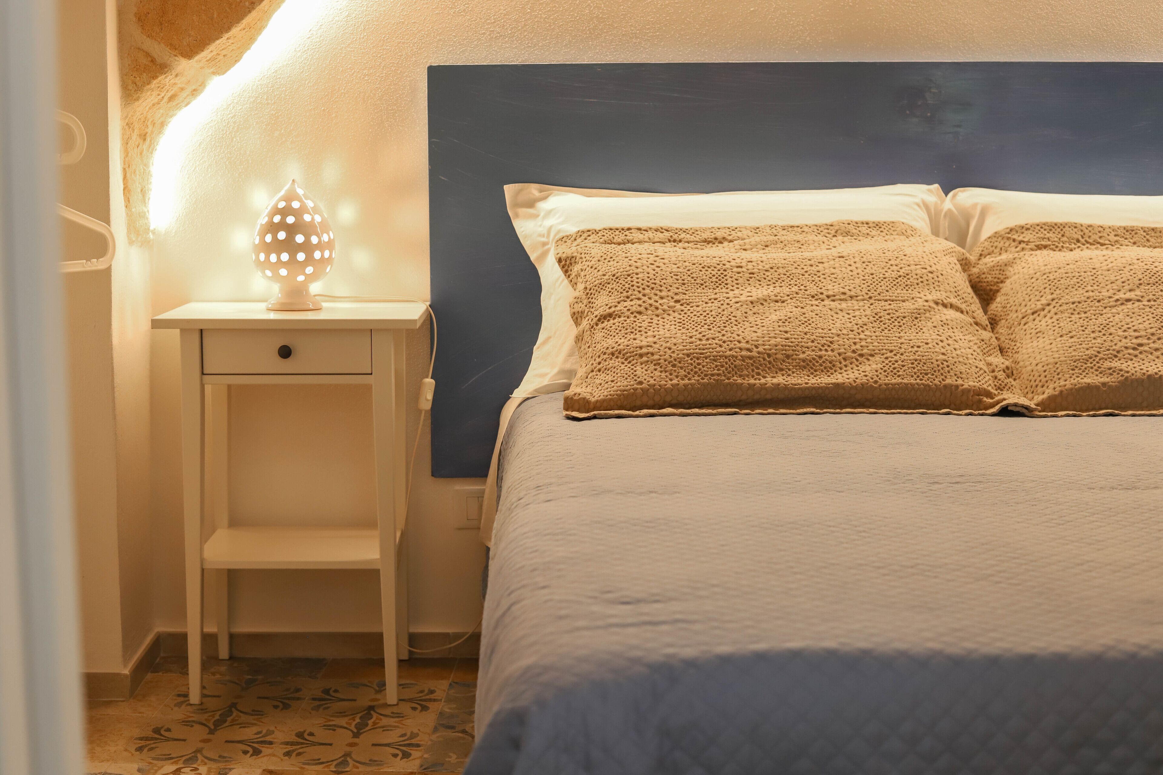 A neatly made bed with a blue headboard, a bedside table with a lamp, and a small drawer.