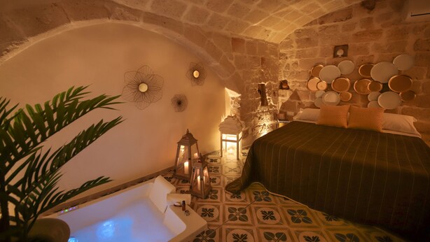 A cozy bedroom with a stone ceiling, a bed with a striped bedspread, a bedside table with a lamp, and a wall-mounted plate rack.