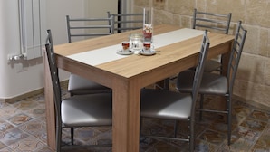 A dining area with a wooden table and metal chairs, a tiled floor, and a stone wall.