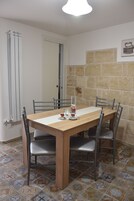 Zona pranzo con tavolo in legno e sedie in metallo, pavimento piastrellato e parete in pietra.