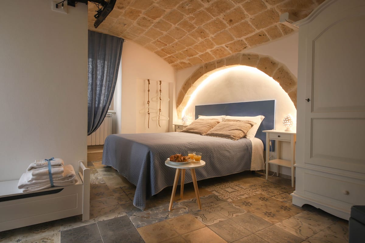 A bedroom with a bed, a bedside table, a small stool, and a nightstand.