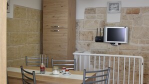 A dining area with a wooden table, metal chairs, a white radiator, and a mounted television.