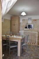 Zona pranzo con tavolo in legno, sedie in metallo, termosifone bianco e televisore a parete.