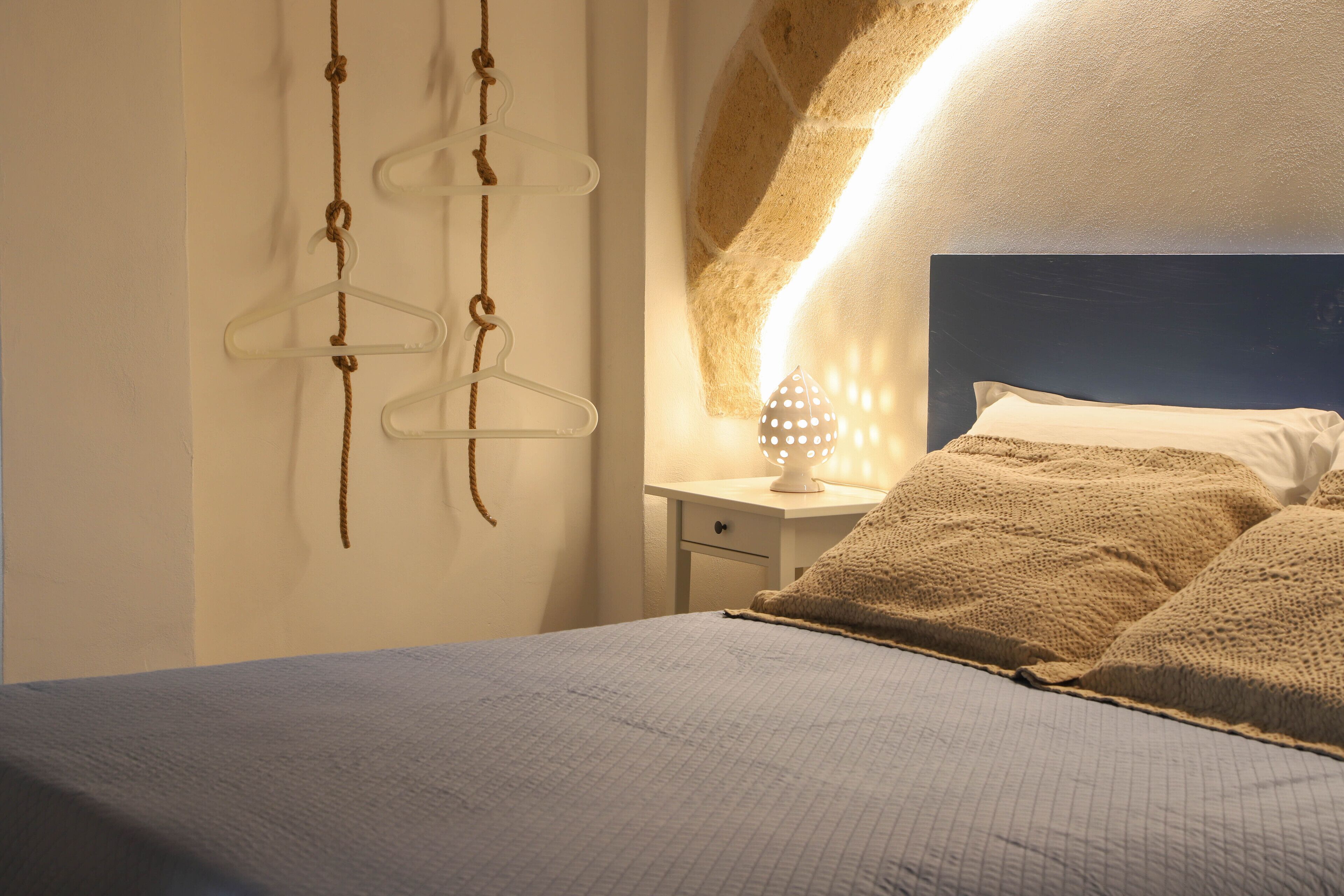 Un dormitorio con una cama, una mesita de noche y un aplique de pared.