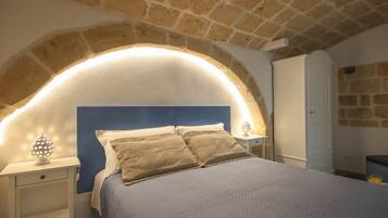 A bedroom with a stone arched ceiling, a bed with a quilted cover, a nightstand with a lamp, and a wardrobe.