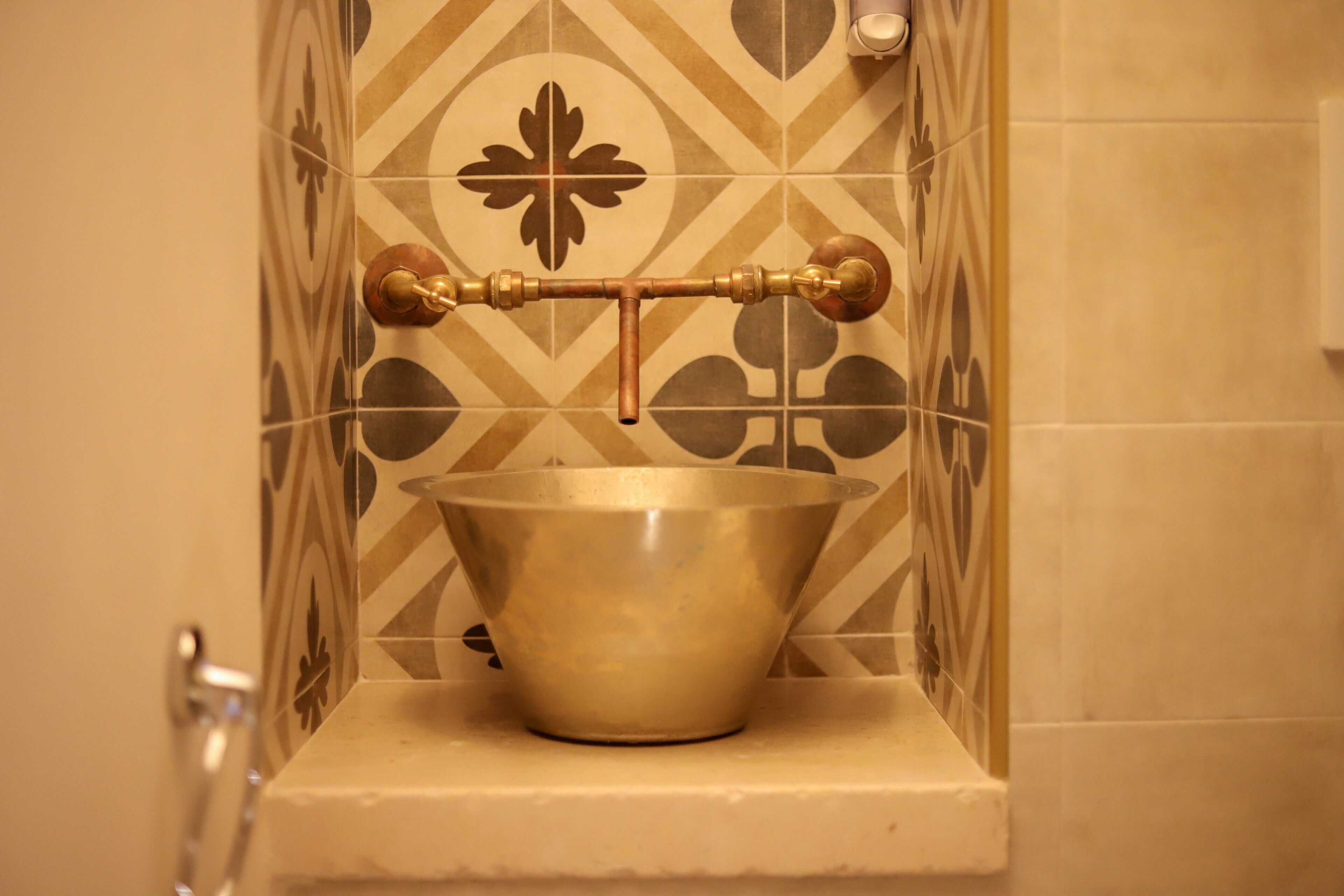 A bathroom with a decorative brass faucet mounted on a tiled wall.