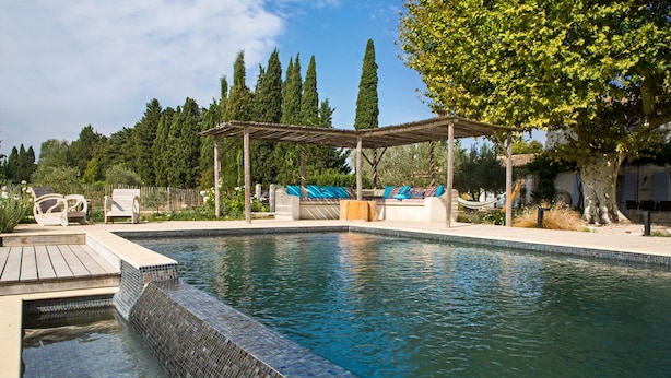 Piscina con borde de azulejos, sillas de descanso y una pérgola.