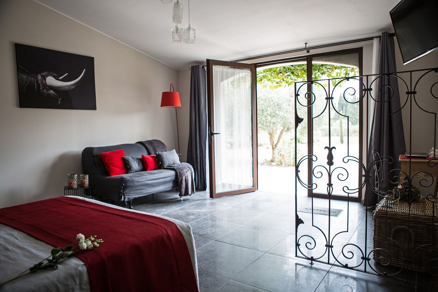 A modern bedroom with a bed, a sofa, a red lamp, and a balcony with a wrought iron gate.
