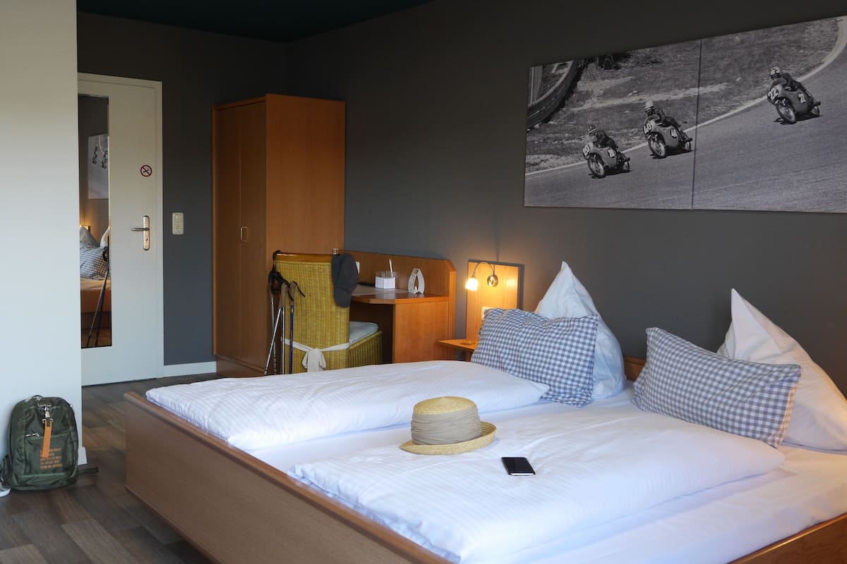 A hotel room with a large bed, a desk, a chair, and a wall-mounted picture of motorcycle racers.