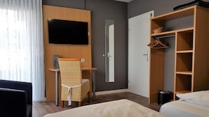 Ett hotellrum med en säng, ett skrivbord, en stol, en garderob och en tv.