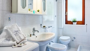 A bathroom with a sink, toilet, and window with a plant. - Casa Maradona (Massa Lubrense)