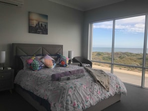 A bedroom with a large bed, a nightstand, a chair, and a view of the ocean.