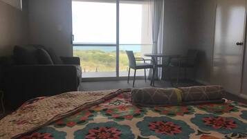 A hotel room with a bed, a small table with chairs, and a balcony with a view of the sea.
