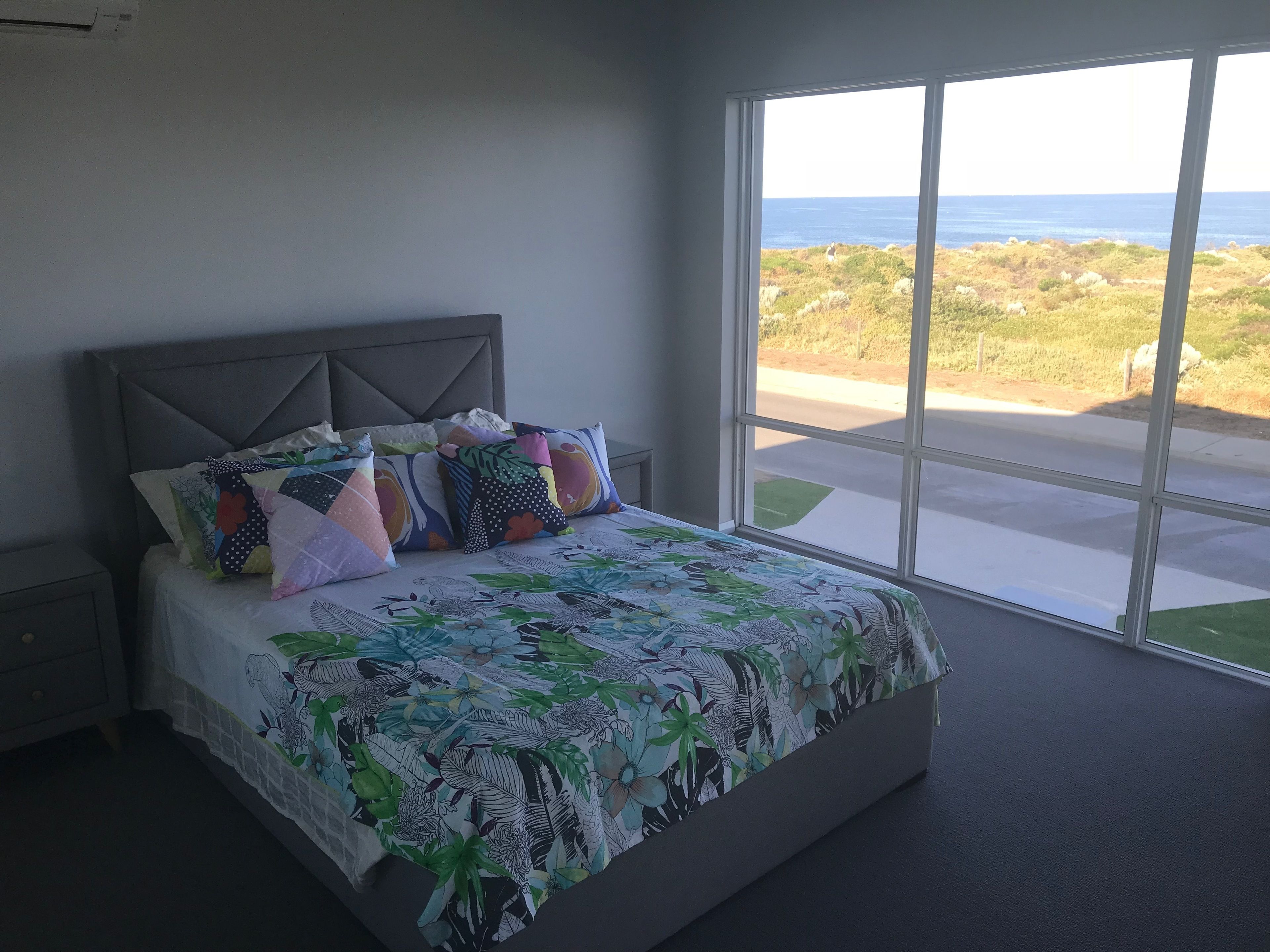 A bedroom with a large bed, a headboard, and a view of the ocean through a window.
