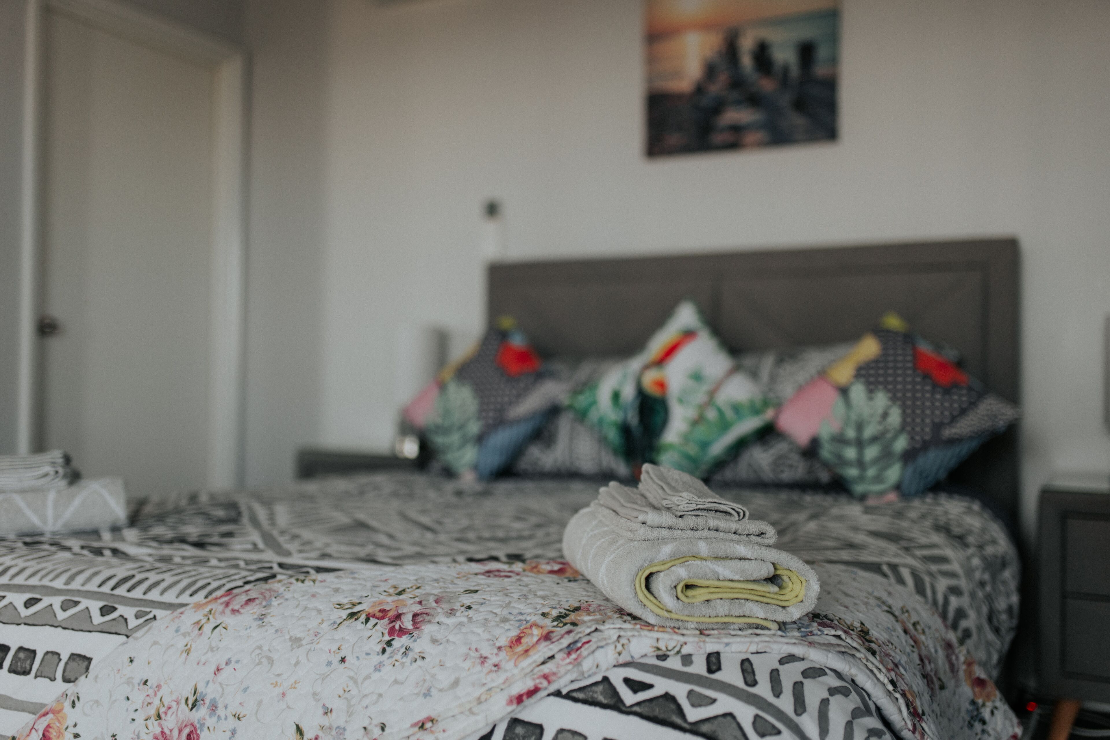 A neatly made bed with patterned bedding and pillows, a bedside table with a lamp, and a painting on the wall.