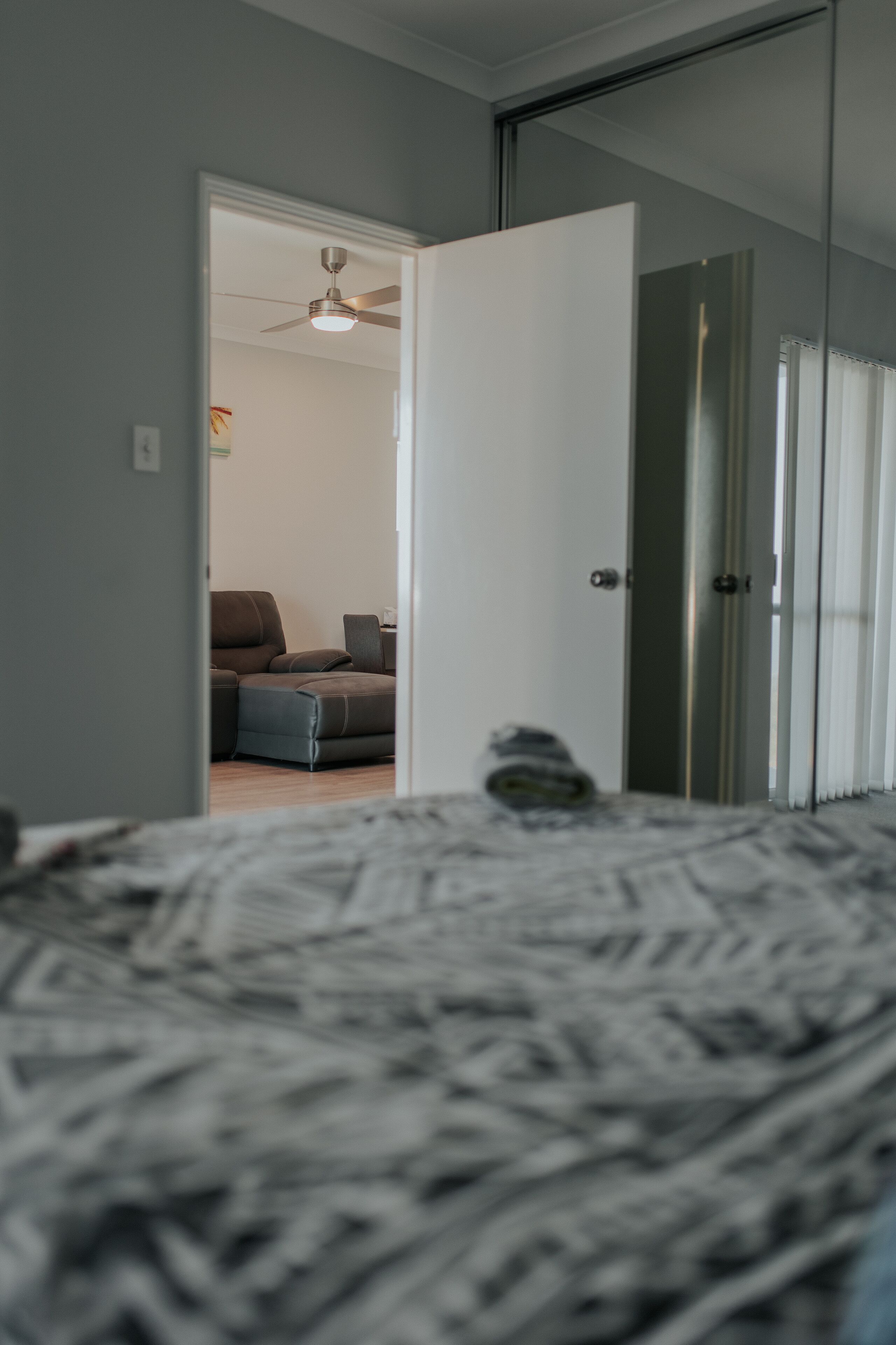 A bedroom with a bed, a door leading to another room, and a ceiling fan.