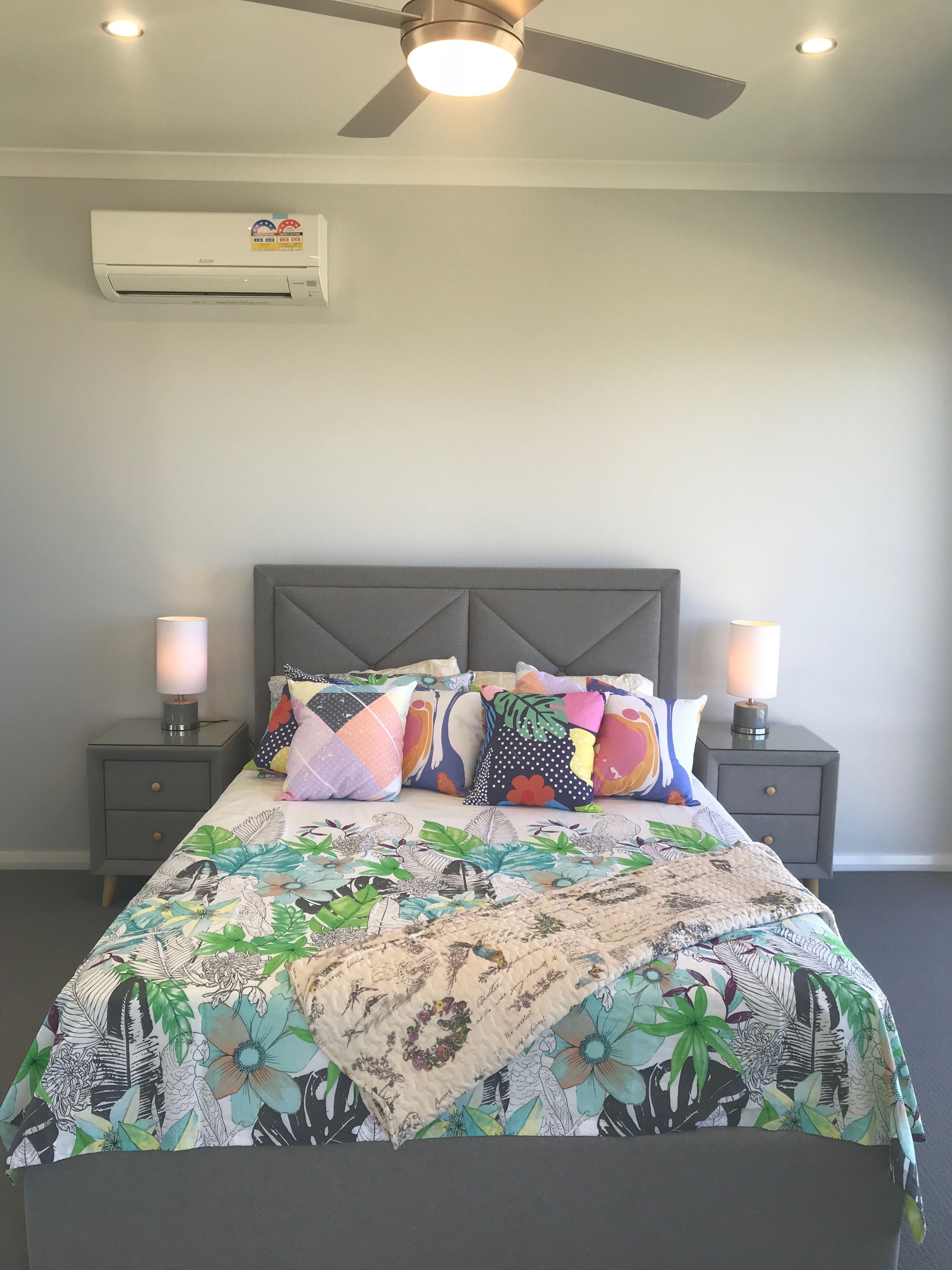 A bedroom with a bed, two bedside lamps, a ceiling fan, an air conditioner, and a wall-mounted air freshener.