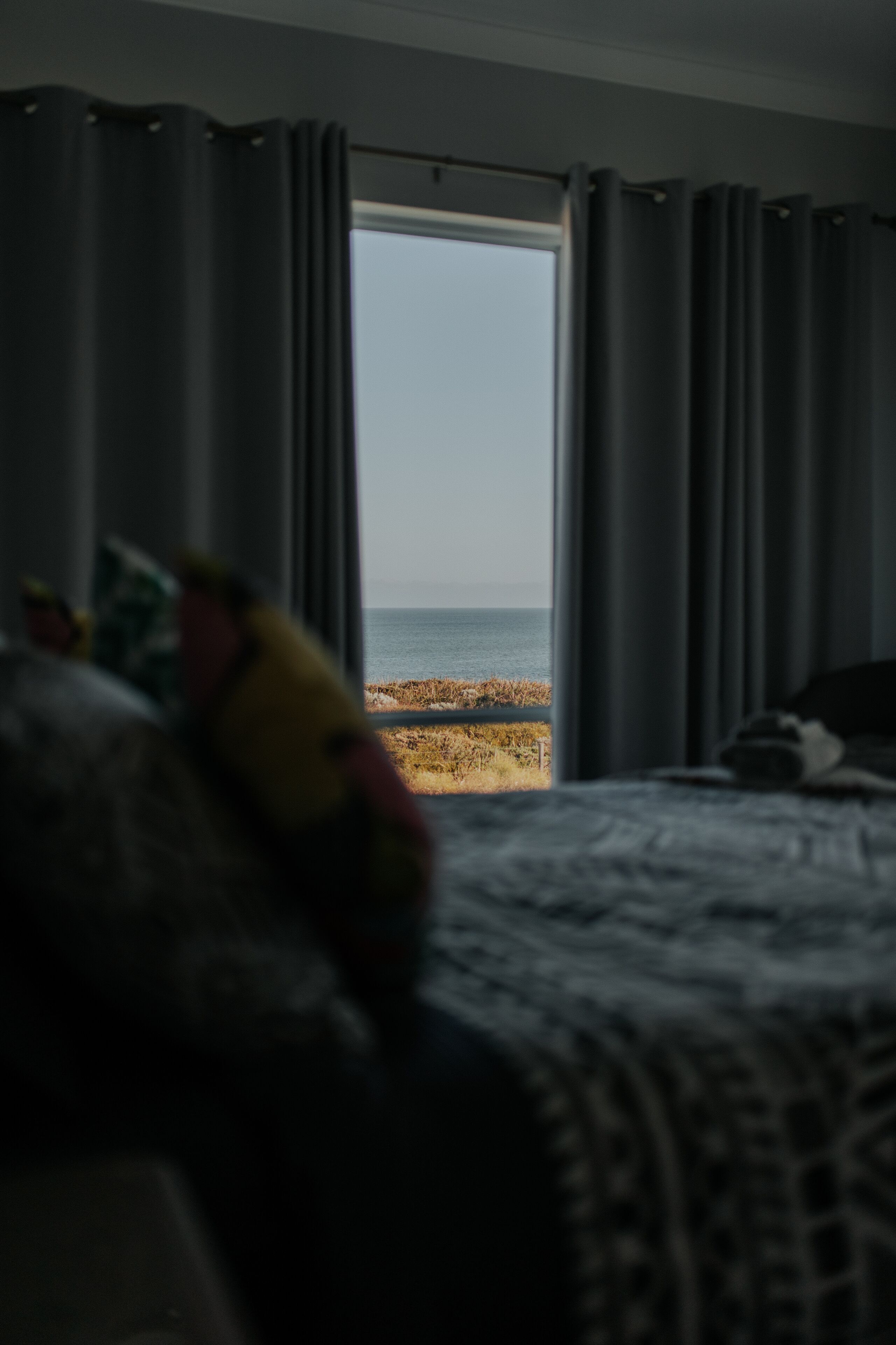 A bedroom with a bed, a window with curtains, and a view of the beach.