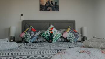 A neatly made bed with patterned bedding, a cityscape painting on the wall, and a nightstand with a lamp.