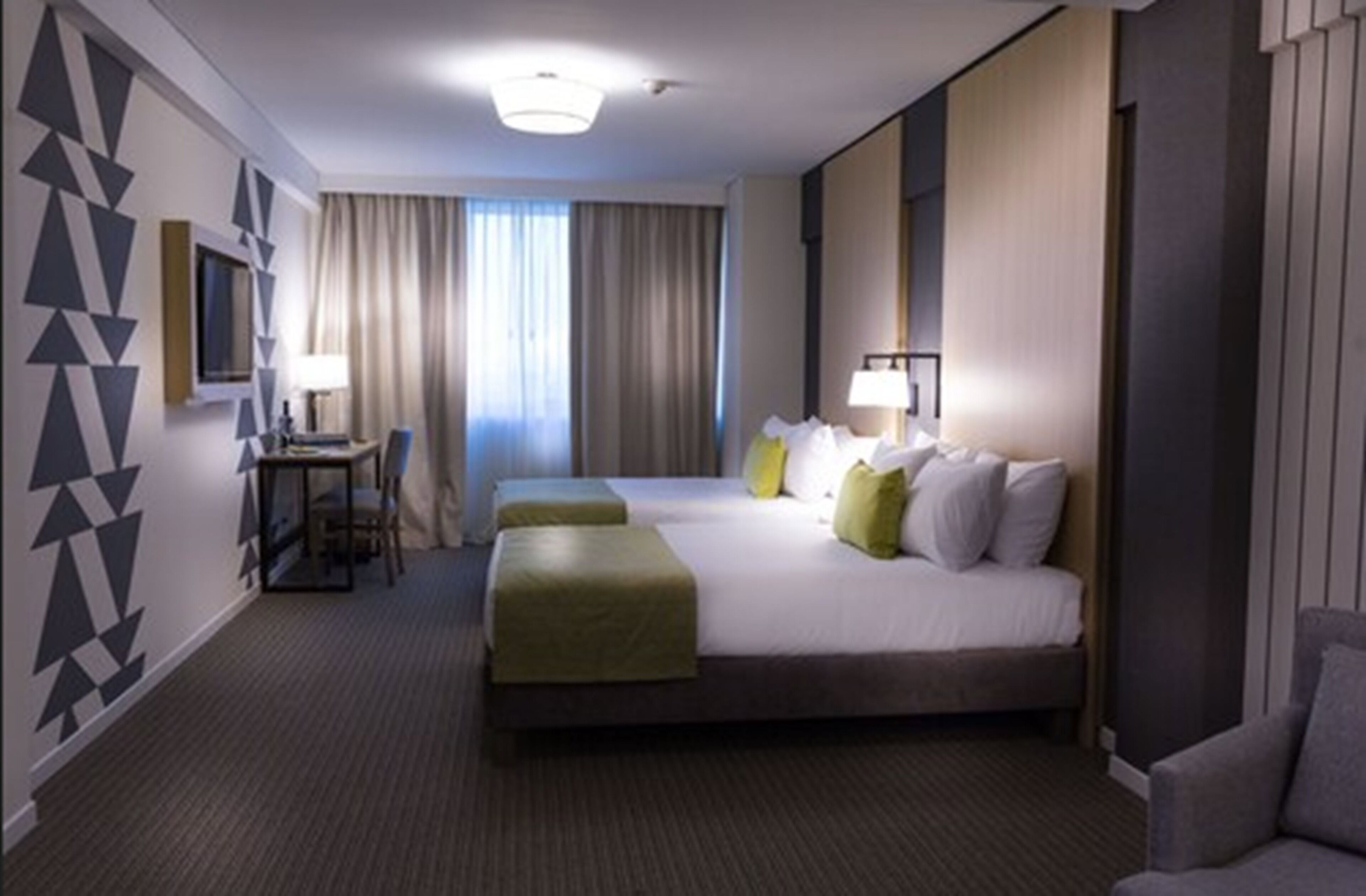 Habitación de hotel con una cama grande, dos mesitas de noche, un escritorio y una silla.
