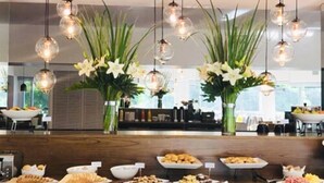 Un aparador de bufet amb diversos aliments i un disseny interior modern que destaca per lluminàries esfèriques penjants i grans composicions florals.