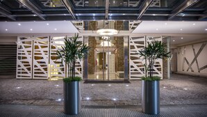 Entrada d'un hotel modern amb una porta de vidre, baranes metàl·liques i plantes en testos.