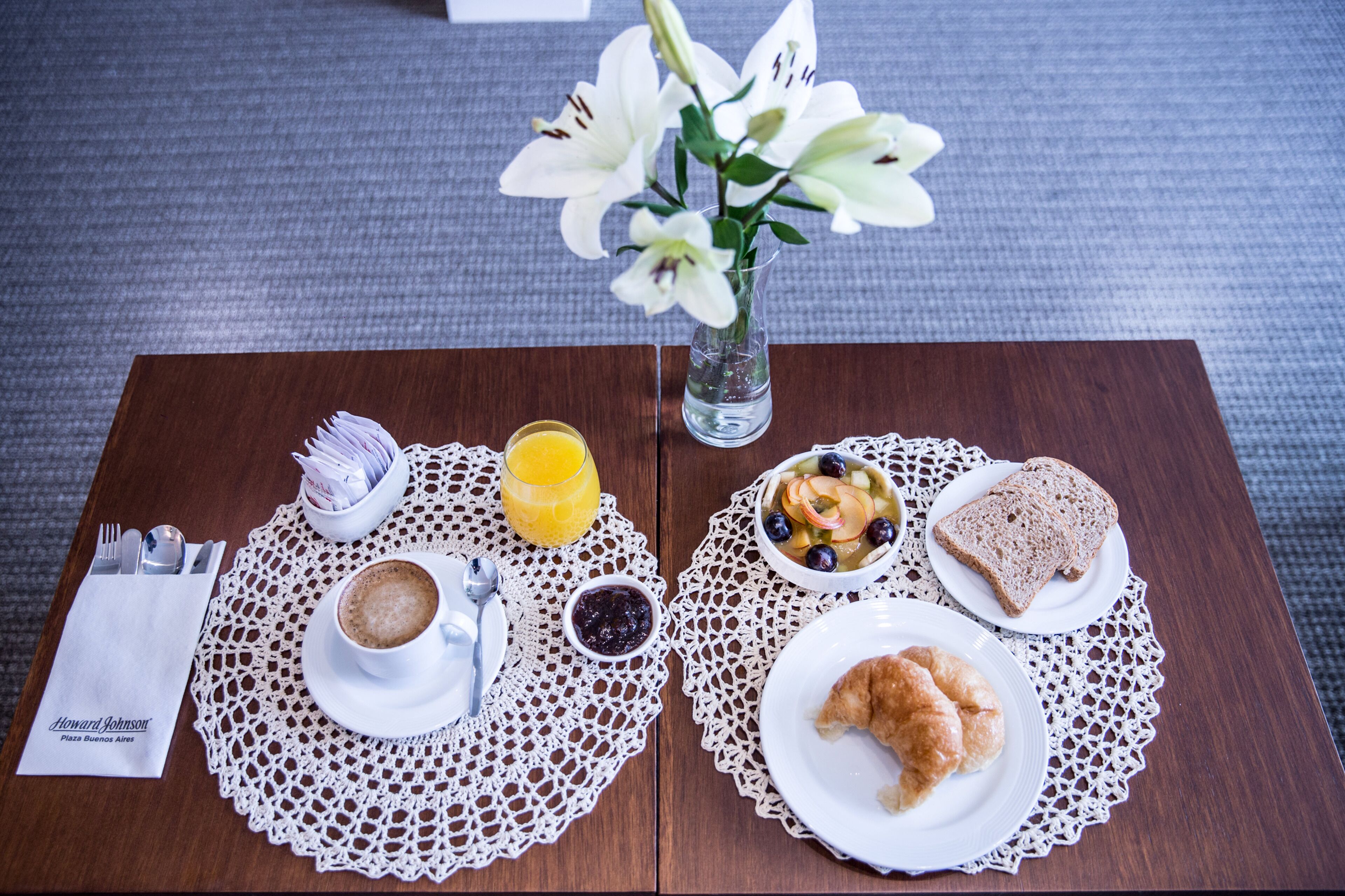 Una mesa de desayuno con un croissant, tostadas, ensalada de frutas, café y jugo.