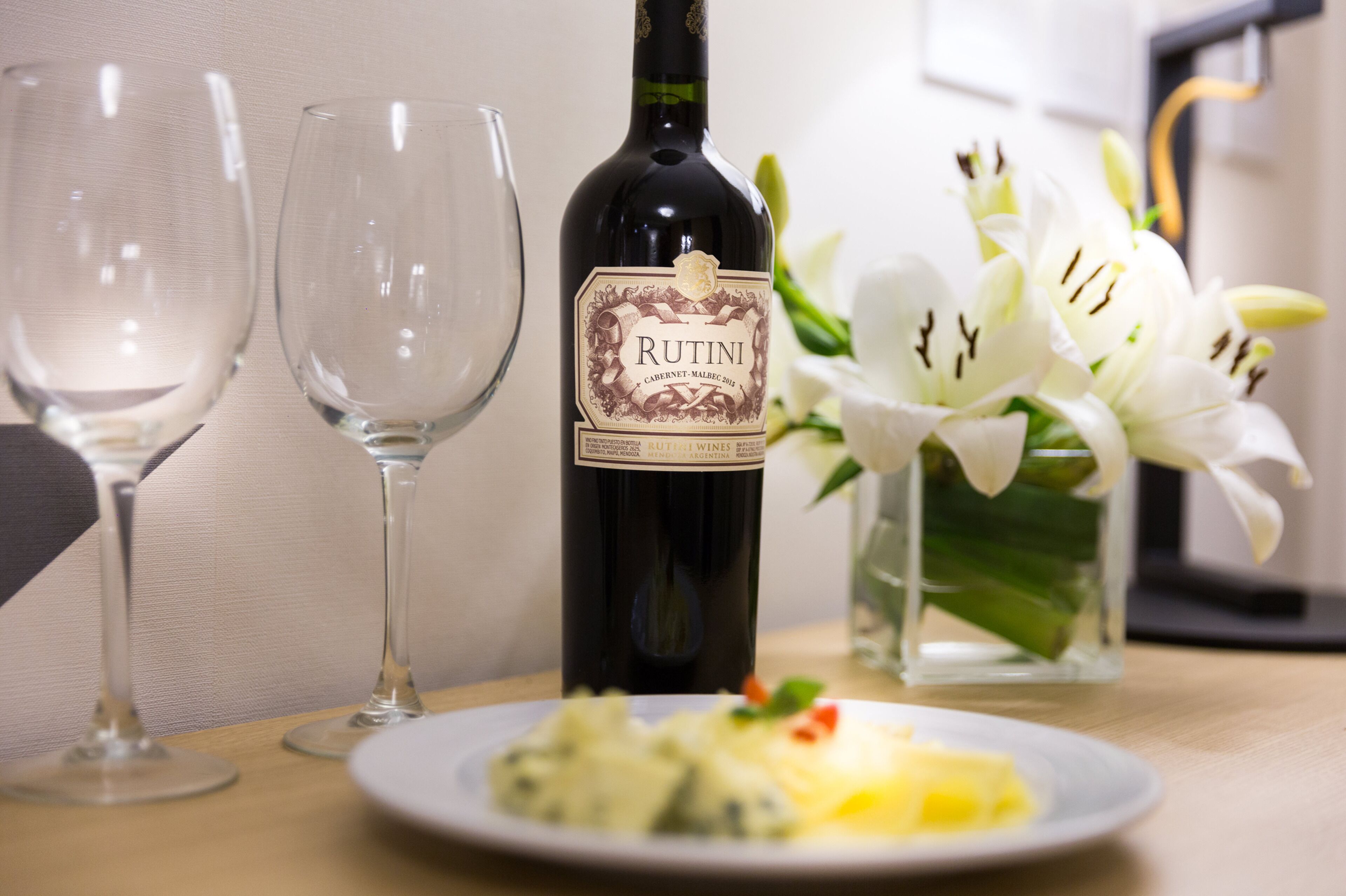 Una botella de vino Rutini, dos copas de vino vacías y un plato con comida sobre una mesa.