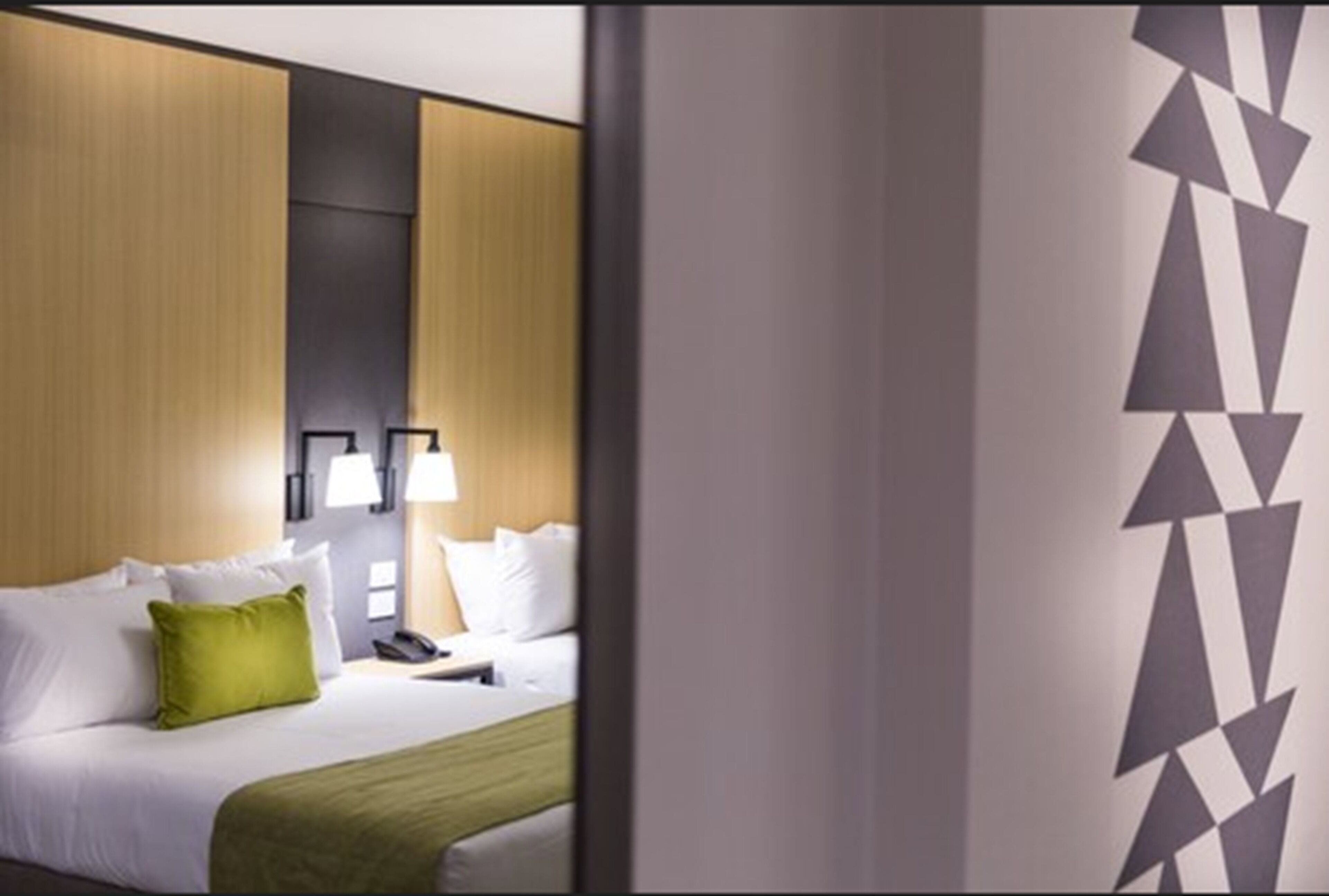 Une chambre d’hôtel avec un lit, des oreillers, une table de chevet et une lampe.