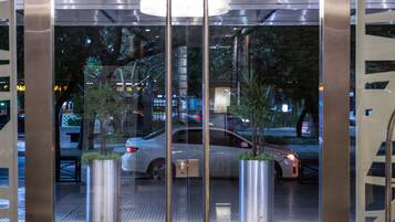 A modern lobby with a glass entrance, a metal staircase, and a central light fixture.