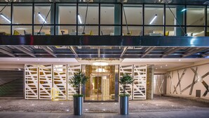 Entrada d'un hotel modern amb façana de vidre, un llum central i dues plantes en testos.
