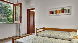 A bedroom with two beds, a window with curtains, a door, and a framed artwork on the wall. - Matisse Cantone (Massa Lubrense)