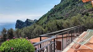 A balcony with two striped lounge chairs, overlooking a coastal landscape with a rocky cliff and a building on the hill. - Matisse Cantone (Massa Lubrense)