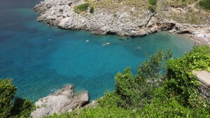 A rocky coastline with clear turquoise waters, a beach area with people, and lush greenery. - Miomar (Massa Lubrense)