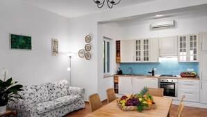 A modern kitchen with white cabinets, a blue backsplash, and a dining area with a wooden table and chairs. - Miomar (Massa Lubrense)