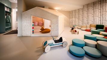 A children's play area with a small house, colorful cushions, and a toy car.