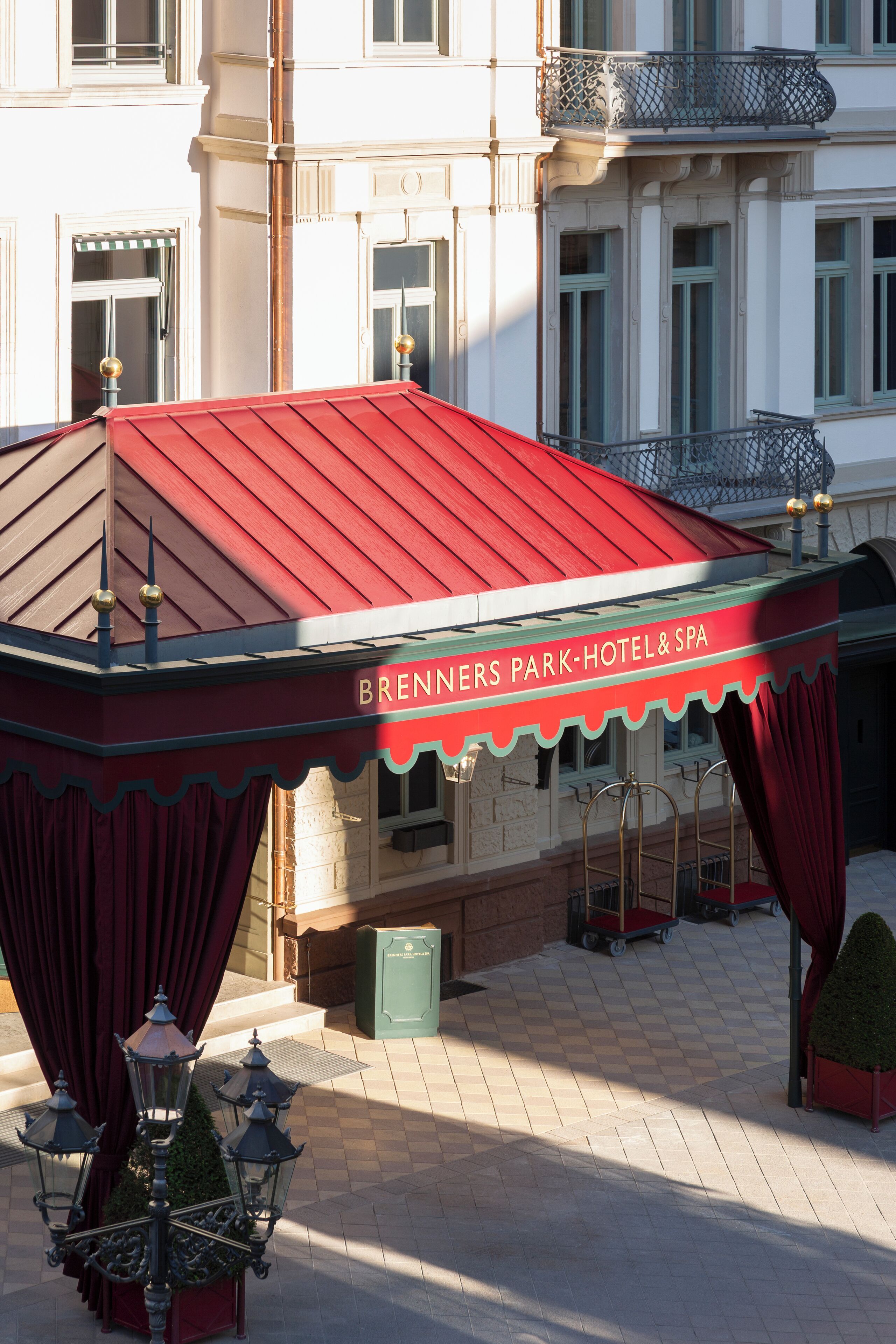 Ein Gebäude mit rotem Dach, mit der Aufschrift "Brenners Park-Hotel & Spa", mit kariertem Boden und einem nahen Mülleimer.