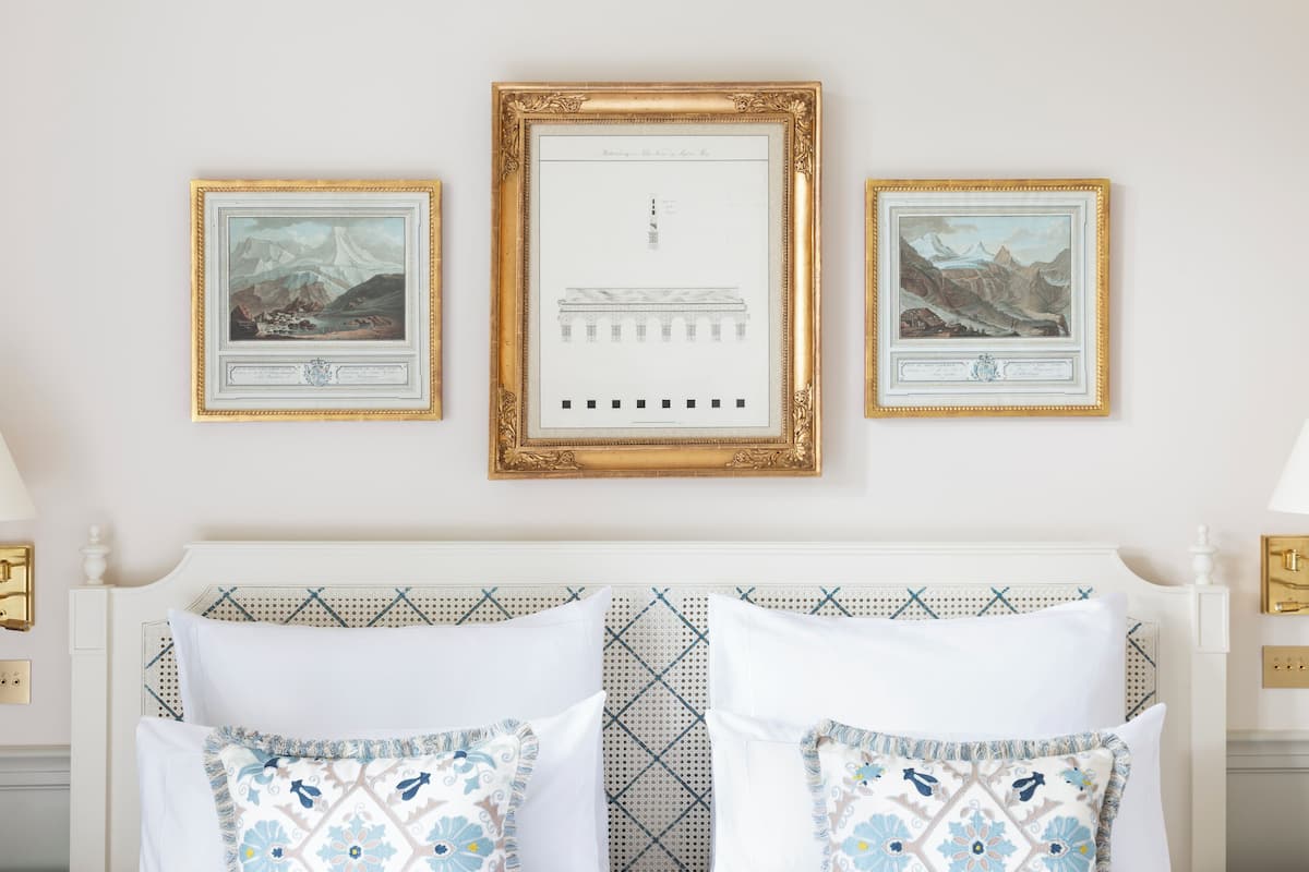 A neatly arranged bedroom with a white bed, patterned pillows, and three framed artworks on the wall.