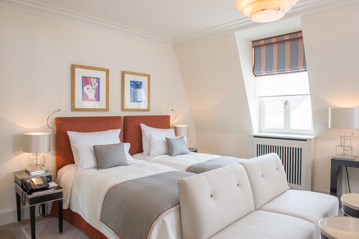 A hotel room with two beds, a sofa, bedside tables with lamps, and framed artwork on the wall.