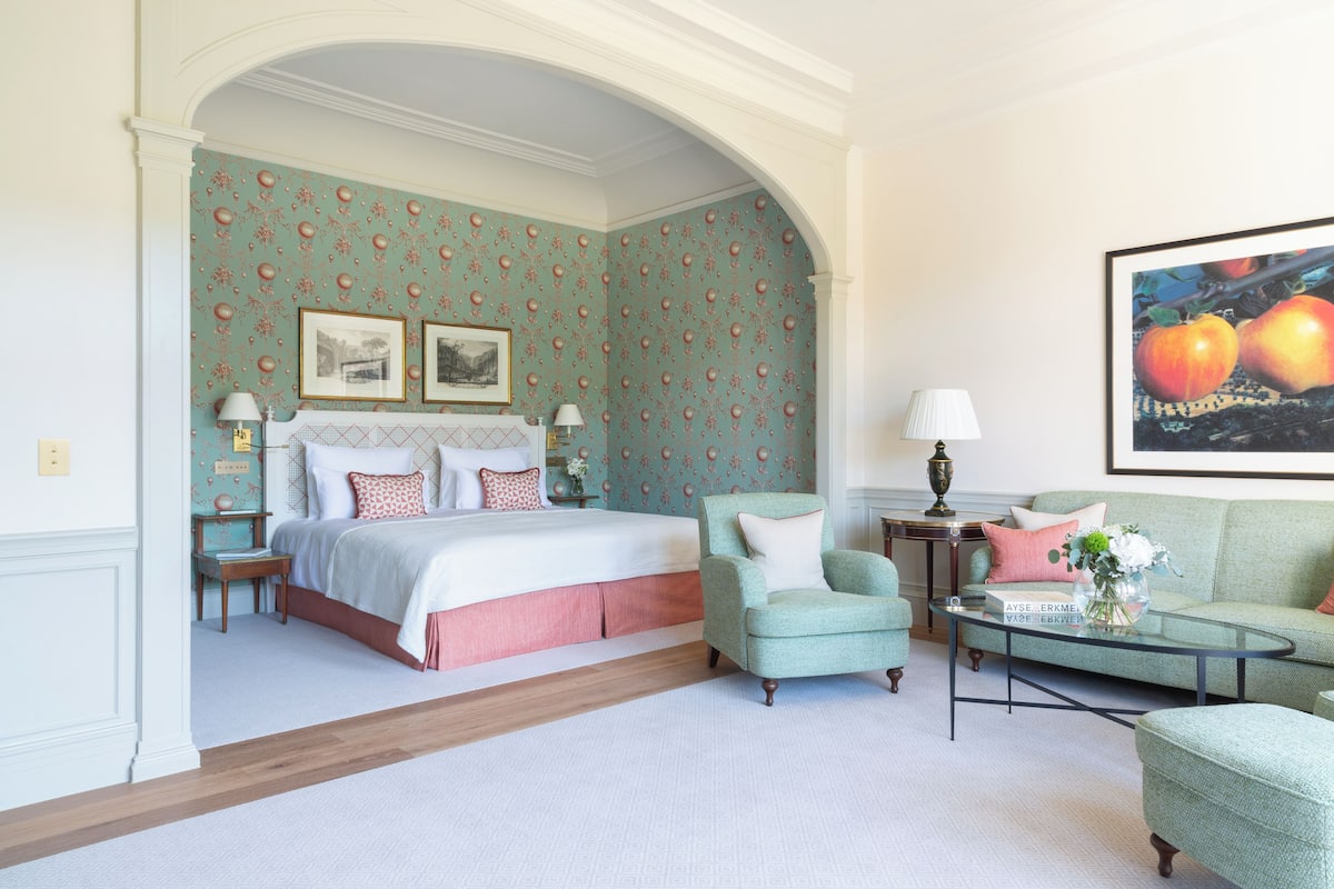 A bedroom with a bed, a chair, a sofa, a coffee table, and a painting.