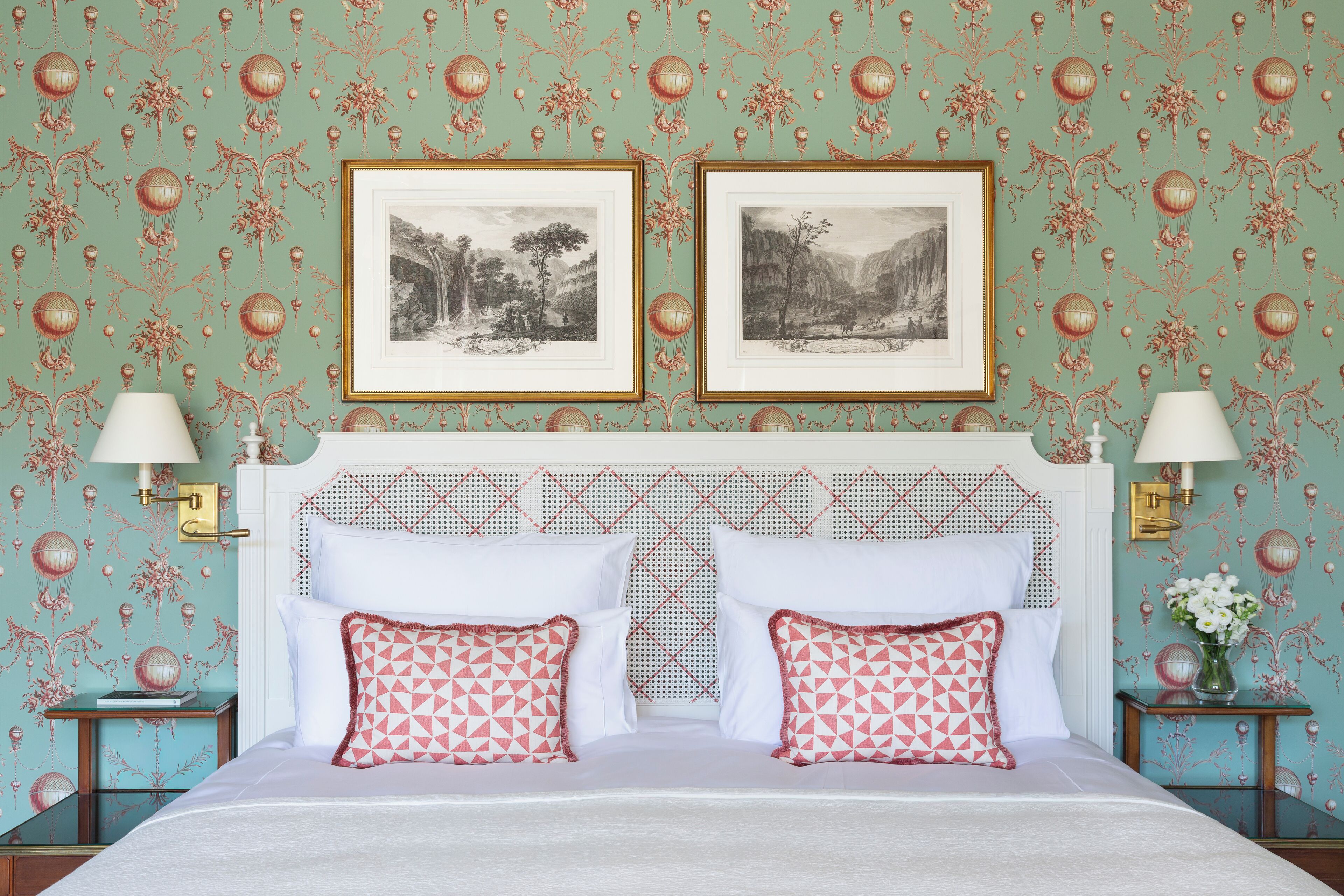 A bedroom with a bed, two framed pictures, two bedside lamps, and a nightstand with a vase.