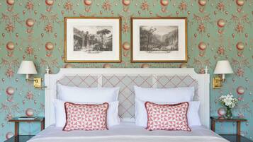 A bedroom with a bed, two framed pictures, two bedside lamps, and a nightstand with a vase.