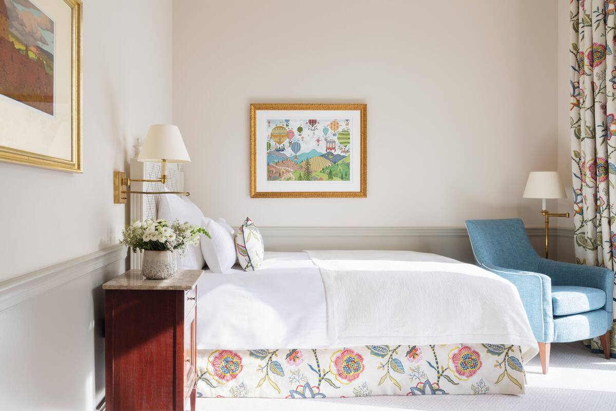 A neatly arranged bedroom with a bed, bedside lamps, a chair, and a framed picture on the wall.