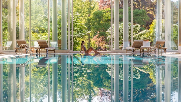 Una piscina amb aigua cristal·lina, envoltada per columnes i cadiretes, amb vista a arbres i vegetació.