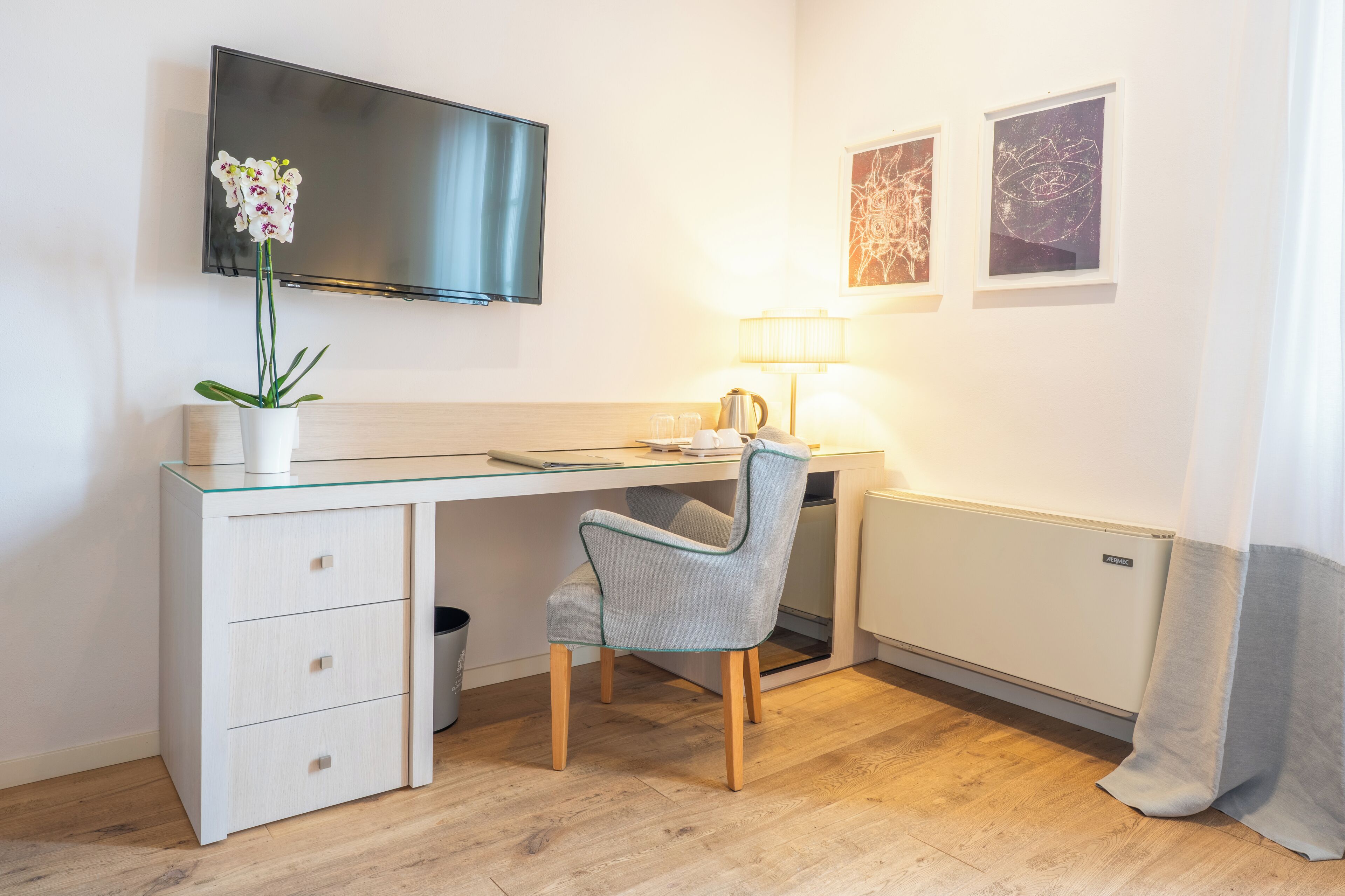 A modern hotel room with a desk, chair, TV, and artwork on the wall.