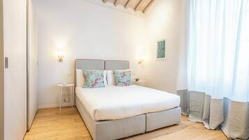 Une chambre à coucher comprenant un lit, des tables de chevet, une commode, une lampe fixée au mur et une fenêtre avec des rideaux.